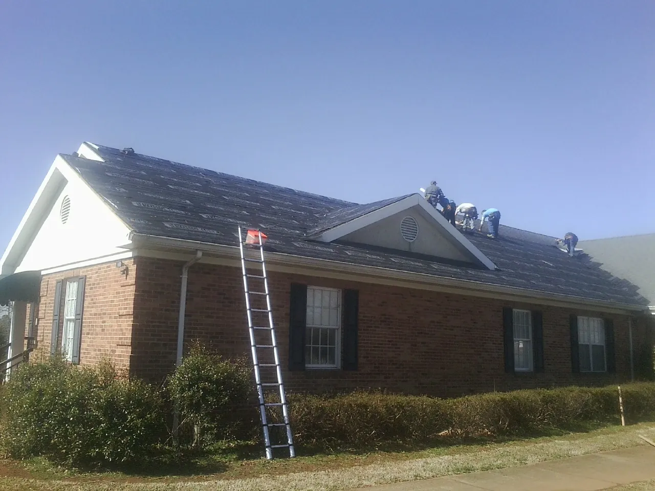 Crew tearing shingles off a brick ranch roof with a ladder set — Emergency Roof Repair work by our crew in Ludlow