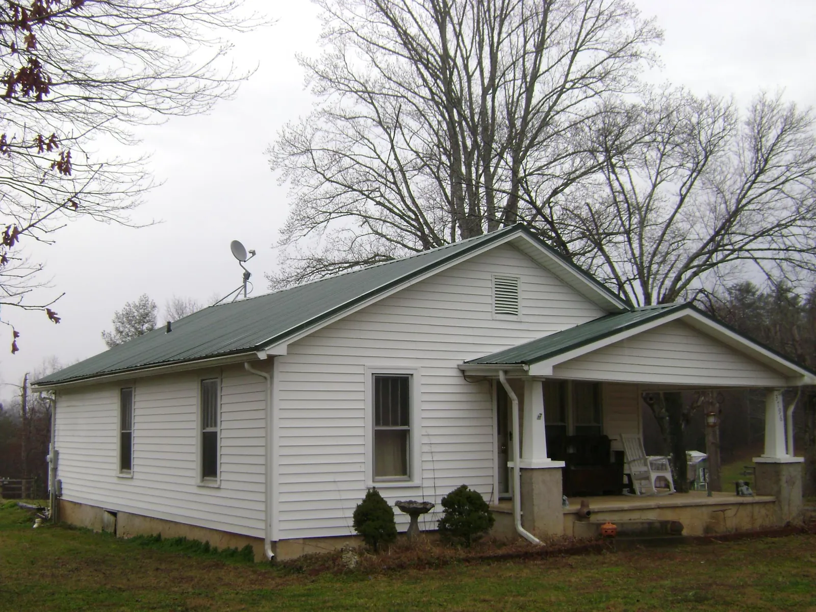 Green metal roof on a white bungalow with a side porch in Ludlow