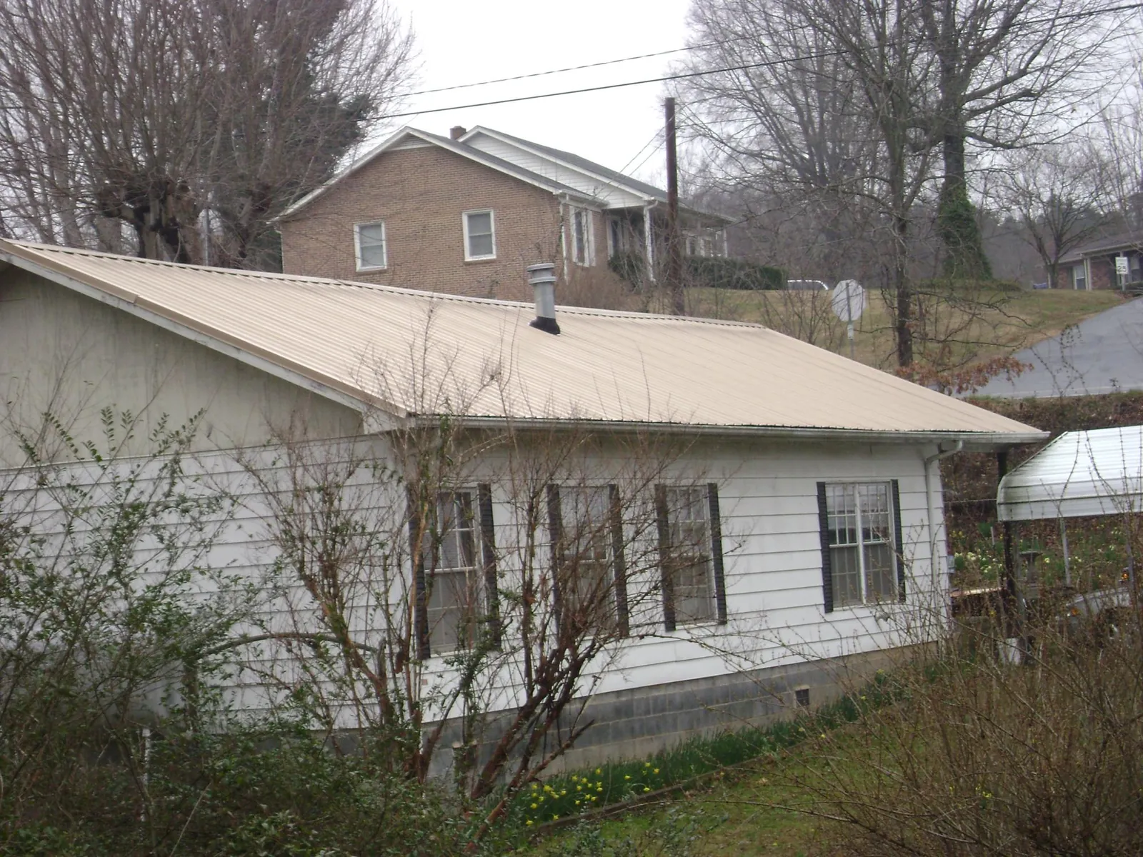 Tan metal roof on a white sided house set into a hillside — Commercial Roofing by Roofing Brothers in Ludlow